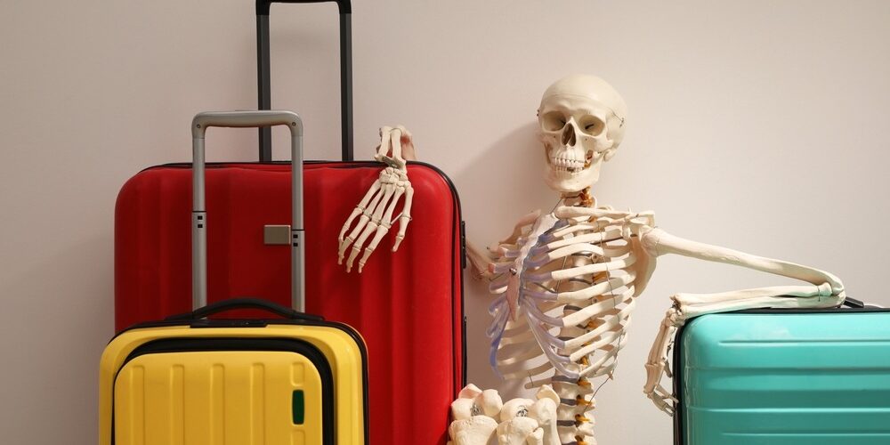 Waiting,Concept.,Human,Skeleton,With,Suitcases,Near,Light,Grey,Wall Halloween Spooky Travel